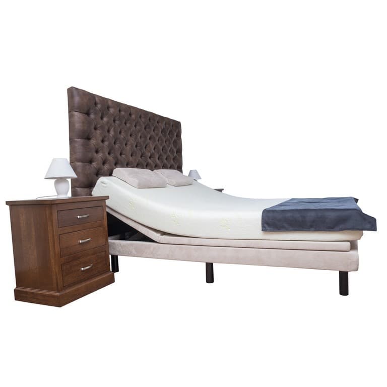 An adjustable bed with the head section raised beside a timber bedside table
